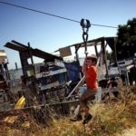 Các khu vui chơi mạo hiểm dành cho trẻ em Trẻ trai mặc áo cam trượt zipline trên khung cáp, phía trước các công trình gỗ tạm bợ trong khu vui chơi mạo hiểm